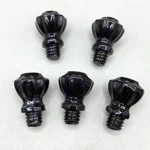 May include: Five black, decorative knobs with a faceted, rounded top and threaded base. The knobs are arranged on a white surface, showcasing their glossy finish and symmetrical design. These knobs are suitable for furniture or other decorative applications.
