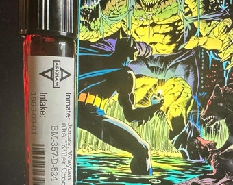 Peut inclure: Une petite bouteille en verre transparent avec un bouchon noir et une étiquette avec du texte. L'étiquette comprend le mot "ARKHAM" et le texte "Intake: 1983-03-01". Derrière la bouteille se trouve une couverture de bande dessinée avec le titre "BATMAN" et le mot "PRODIGAL".