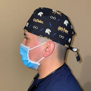 May include: Black and blue surgical scrub hat with a Harry Potter theme. The hat features a Gryffindor lion, lightning bolts, and the words "Harry Potter" and "Gryffindor".