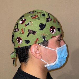 May include: A green surgical scrub hat with a repeating pattern of Freddy Krueger's glove, a fedora hat, and the words "Elm Street" and "Springwood".