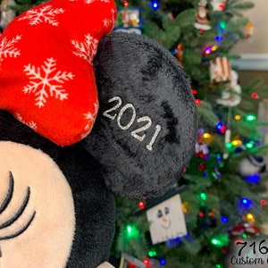 May include: A black and red plush toy with a bow and a black ear with the year 2021 embroidered on it.