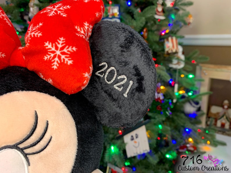 May include: A black and red plush toy with a bow and a black ear with the year 2021 embroidered on it.