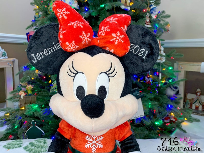 May include: A red and white plush Minnie Mouse Christmas ornament with a red bow and snowflake pattern. The ornament is personalized with the name "Jeremia" and the year "2021".