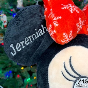 May include: Personalized black and red Minnie Mouse ears with a white snowflake pattern and the name "Jeremiah" embroidered on the black ear.