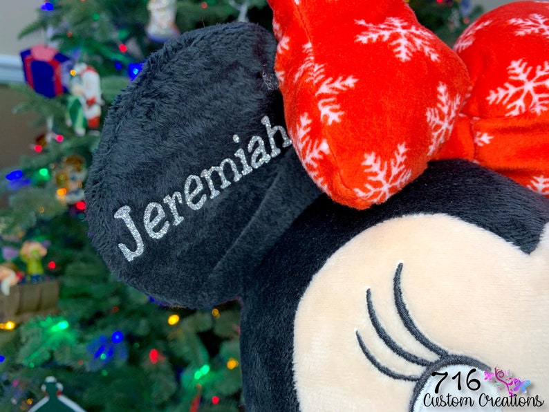 May include: Personalized black and red Minnie Mouse ears with a white snowflake pattern and the name "Jeremiah" embroidered on the black ear.