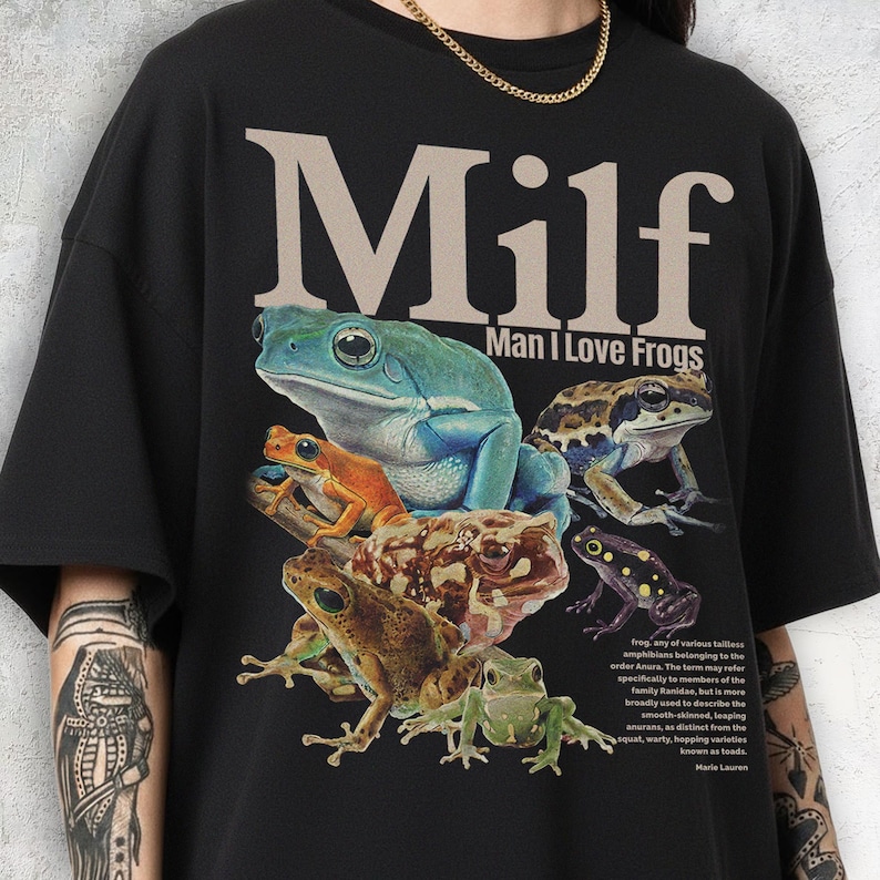 May include: Black t-shirt featuring a colorful graphic of several frogs. The text "Milf Man I Love Frogs" is printed above the frogs. A small paragraph about frogs is printed below the frogs.