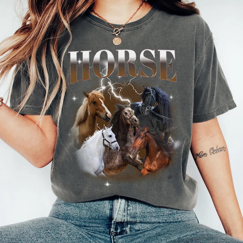 May include: A dark gray t-shirt with the word "HORSE" printed in silver letters. The shirt features a graphic of five horses in a variety of colors and poses, with a lightning bolt design behind them.