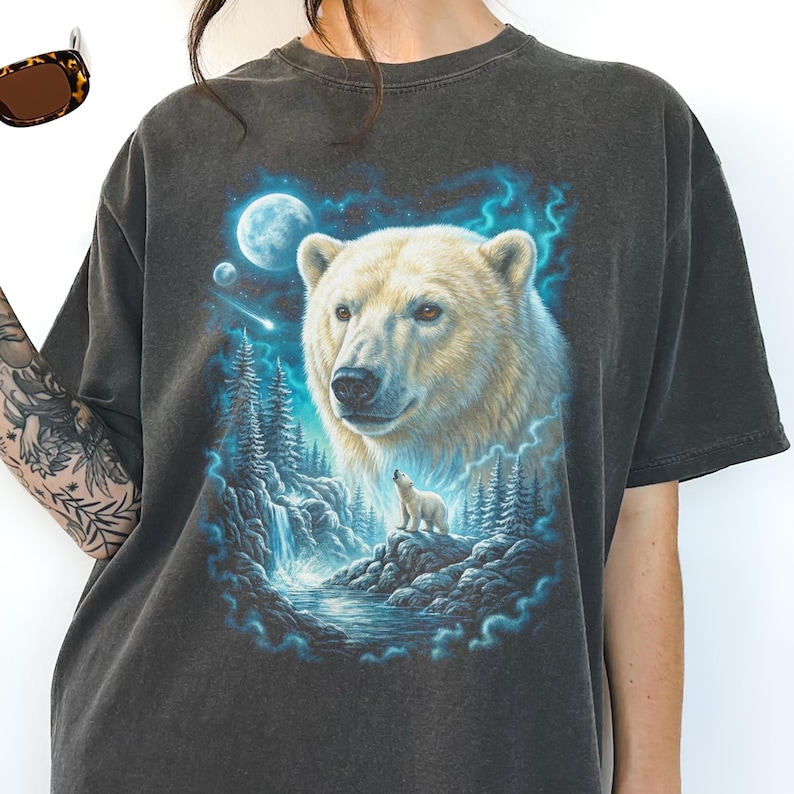 May include: Dark grey t-shirt with a detailed illustration of a polar bear and cub, set against a moonlit forest and waterfall. The design incorporates shades of blue and white, creating a serene, nature-themed graphic.