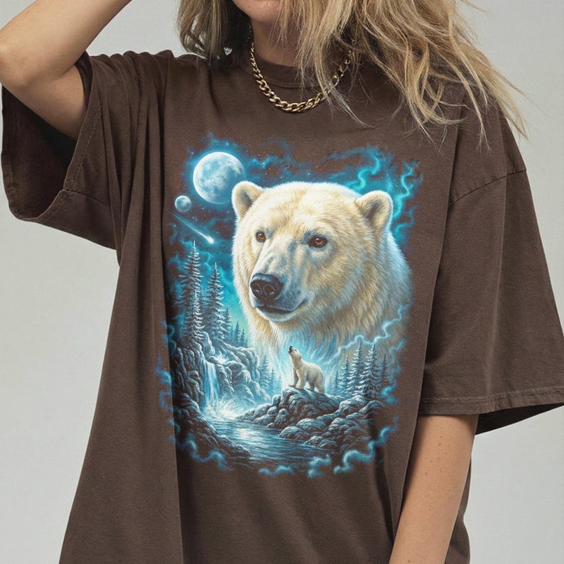 May include: Brown t-shirt with a detailed illustration of a polar bear and cub in a forest scene under a full moon. The artwork includes a waterfall, trees, and blue accents, creating a nature-themed design.