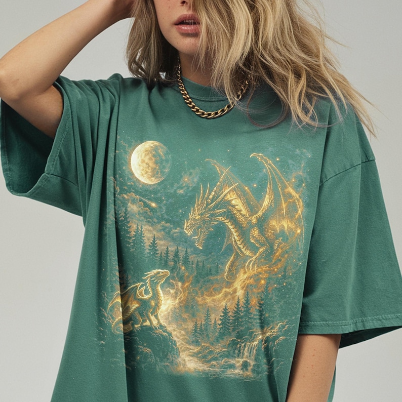 May include: Green t-shirt featuring a fantasy scene with two dragons, a full moon, and a forest. The larger dragon is golden, with the smaller one perched on a rock. The design has a mystical, ethereal quality.