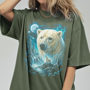 May include: An olive green t-shirt with a detailed illustration of a polar bear and cub in a moonlit forest with a waterfall. The bear's fur is creamy white, and the scene is framed by blue and teal accents.