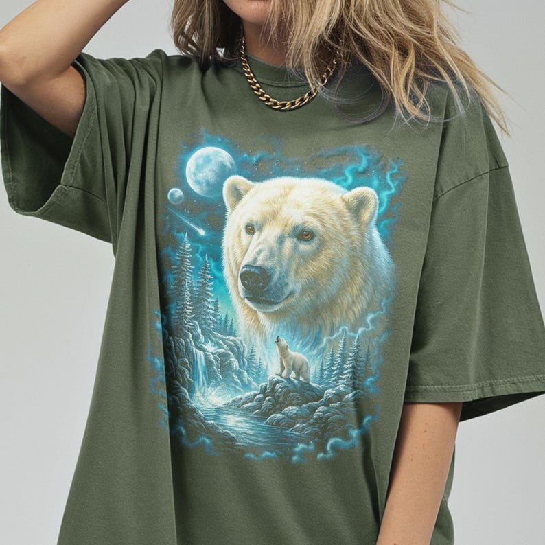 May include: An olive green t-shirt with a detailed illustration of a polar bear and cub in a moonlit forest with a waterfall. The bear's fur is creamy white, and the scene is framed by blue and teal accents.