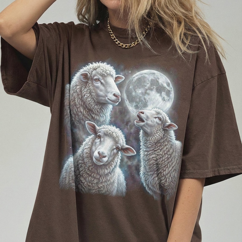 Puede incluir: Camiseta marr&oacute;n con un gr&aacute;fico de tres ovejas y una luna llena. Las ovejas est&aacute;n en blanco y gris, con texturas de lana detalladas. La luna es un orbe brillante en el fondo. Corte holgado.