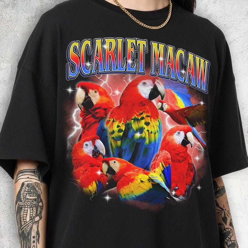 May include: Black t-shirt featuring a vibrant graphic of scarlet macaws with red, yellow, and blue plumage. The text "SCARLET MACAW" is arched across the top in a retro font, with a lightning bolt background.