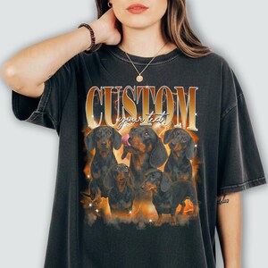 May include: Dark grey t-shirt with a graphic of six dachshund dogs. The word "CUSTOM" is in gold and orange, with "your text" below. The dogs are black and brown, with one licking its nose.