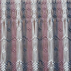 May include: Macrame wall hanging in a geometric pattern. The piece features alternating vertical stripes of gray, white, and mauve. The macrame is suspended from a wooden dowel, creating a decorative textile for home decor.
