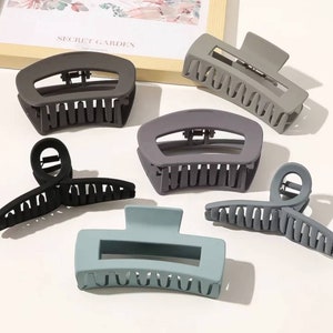 May include: Assortment of six hair clips in various colours, including black, grey, and blue. The clips are made of plastic and have a claw-like design.