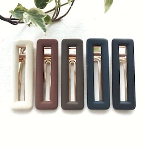 May include: Five rectangular hair clips in different colours: white, brown, dark brown, dark blue, and black. Each clip has a gold metal spring.