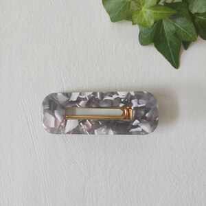 May include: A gray and white marbled hair clip with a gold metal spring.
