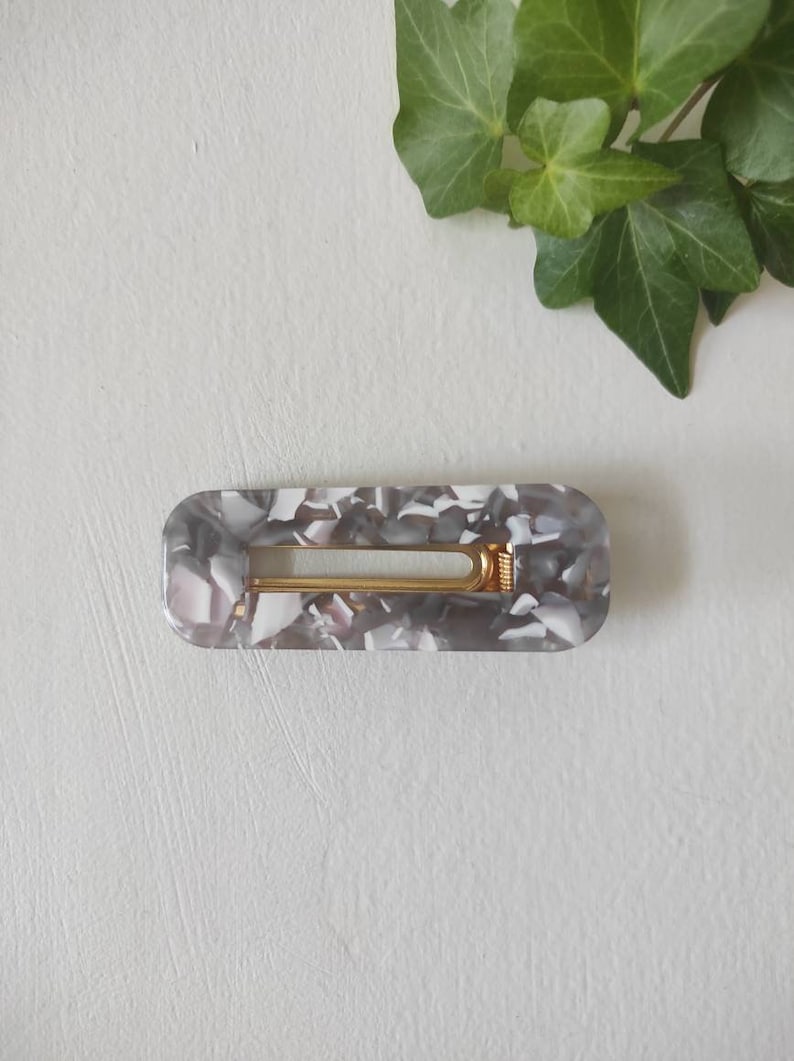 May include: A gray and white marbled hair clip with a gold metal spring.