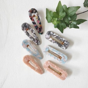 May include: Set of seven colorful hair clips with a marbled pattern. The clips are made of plastic and have a gold metal spring.
