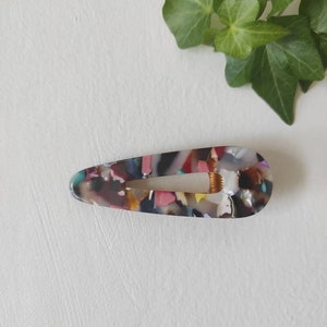 May include: A colorful, multi-colored, teardrop-shaped hair clip with a mottled pattern.