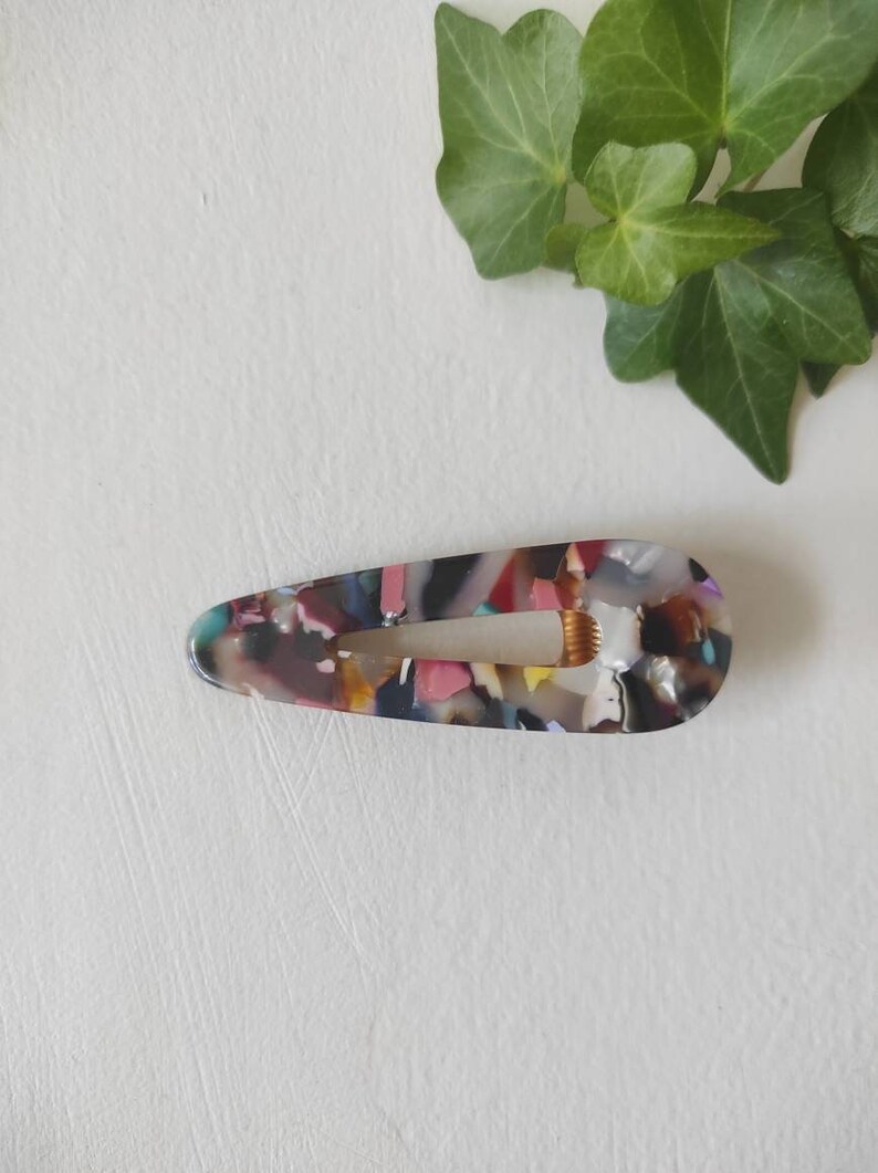 May include: A colorful, multi-colored, teardrop-shaped hair clip with a mottled pattern.