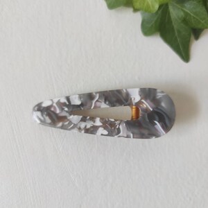 May include: A gray and white marbled hair clip with a gold metal clasp.