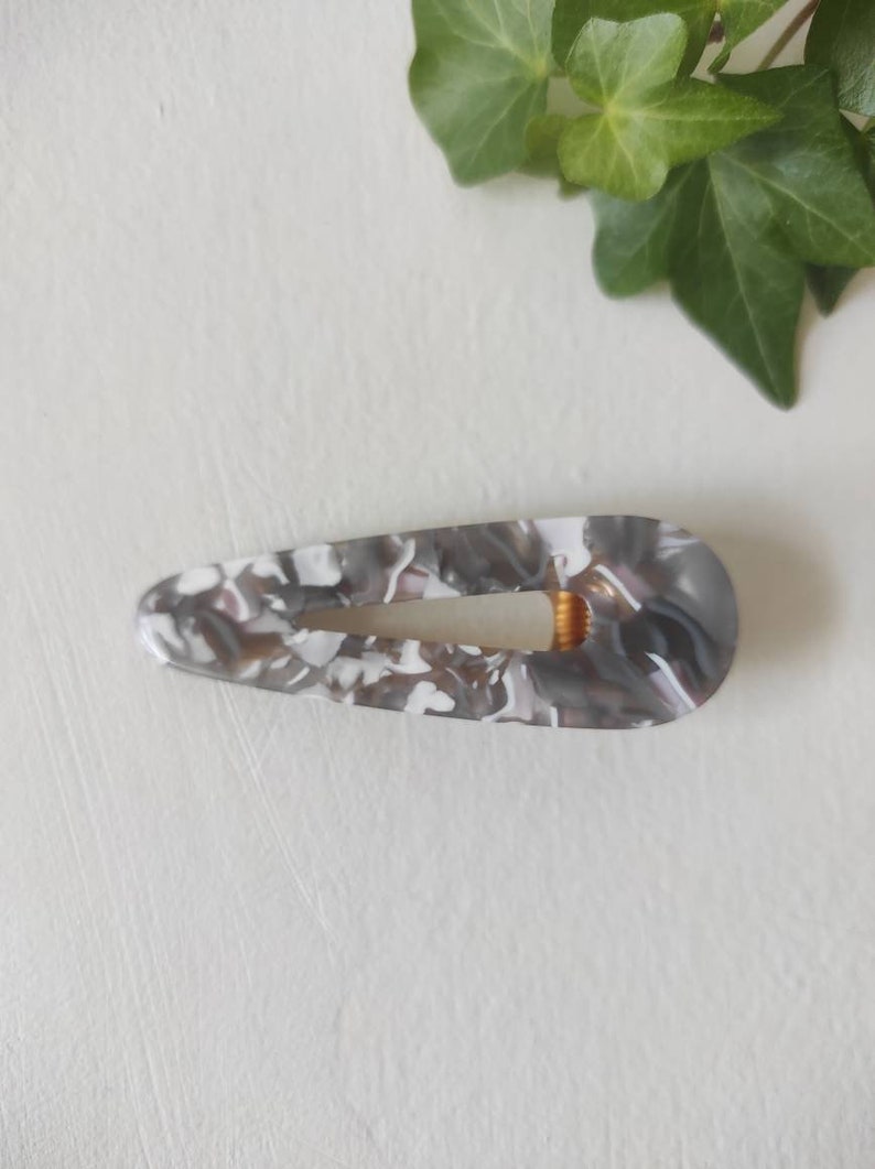 May include: A gray and white marbled hair clip with a gold metal clasp.