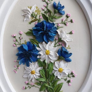 Puede incluir: Una pintura enmarcada de un ramo de flores azules y blancas. Las flores est&aacute;n pintadas en un estilo realista con pinceladas texturizadas. El fondo es de color beige claro.