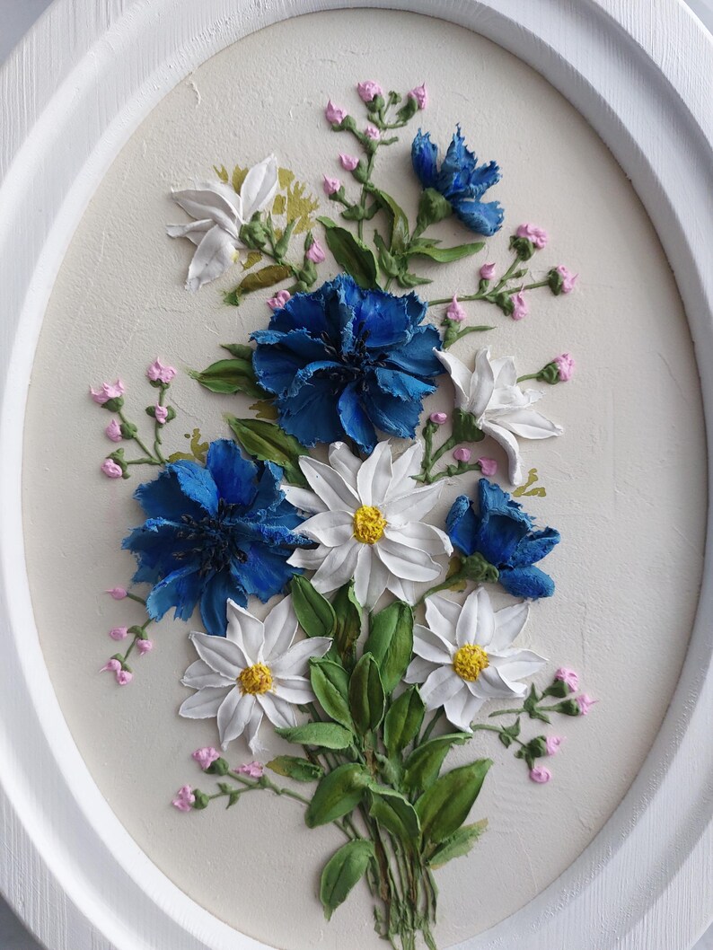 Puede incluir: Una pintura enmarcada de un ramo de flores azules y blancas. Las flores est&aacute;n pintadas en un estilo realista con pinceladas texturizadas. El fondo es de color beige claro.
