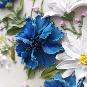 Puede incluir: Primer plano de una flor azul con p&eacute;talos blancos y un centro amarillo. La flor est&aacute; rodeada de hojas verdes y otras flores.