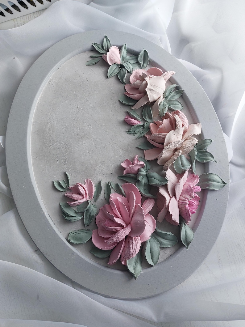 May include: Oval, gray decorative tray with raised floral design. The flowers are pink and the leaves are green. The tray is approximately 12 inches in diameter.