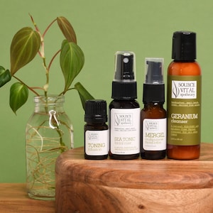 Puede incluir: Una colección de productos para el cuidado de la piel, que incluye una bruma facial, una loción y un limpiador, expuestos sobre una superficie de madera. Los frascos son de varios tamaños y formas, con etiquetas que muestran el nombre de la marca y la información del producto.