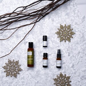 May include: Four small bottles of essential oils and a lotion bottle on a white surface with gold snowflake decorations. The bottles are labelled "Clear Skin", "Aromatic", "Algae Deep", and "Rose & Frankincense".