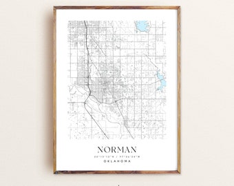 May include: A black and white map print of Norman, Oklahoma with the city name and coordinates in the bottom right corner. The map is framed in a light brown wood frame. The text "modern" is below the frame and the text "www.etsy.com/shop/ElegantMaps" is below that.