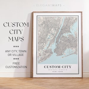 May include: A framed map of New York City with a light blue background and black lines showing streets and waterways. The text "CUSTOM CITY" is at the bottom of the map with the coordinates "40 42 46' N / 74 00 21' W" and "NEW YORK". The text "CUSTOM CITY MAPS" is at the top left of the image with the text "ANY CITY, TOWN OR VILLAGE" and "FREE CUSTOMIZATION" below it.