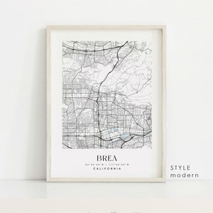 May include: A black and white map print of Brea, California in a white frame. The map shows the city streets and landmarks. The text "BREA" is printed in black at the bottom of the map, along with the coordinates "33°56'24" N / 117°53'26" W" and the word "CALIFORNIA". The text "STYLE modern" is printed in black in the bottom right corner of the frame.