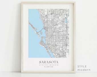 May include: A black and white map of Sarasota, Florida with a light blue outline of the coastline. The map is framed in a white frame and has the text "SARASOTA" and "27 20 14 N / 82 32 07 W" and "FLORIDA" below the map. The text "STYLE modern" is in the bottom right corner of the image.