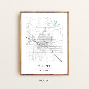 May include: A black and white map of Merced, California with a blue outline of a lake. The map is framed in a light brown wood frame. The text "MERCED 37°18'50"N / 120°38'00"W CALIFORNIA" is printed below the map.
