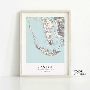 May include: A vintage style map print of Sanibel, Florida. The map is in shades of blue and beige with black lines for roads and waterways. The text "Sanibel, Florida 26.24'23" N / 82.04'50" W" is printed below the map.