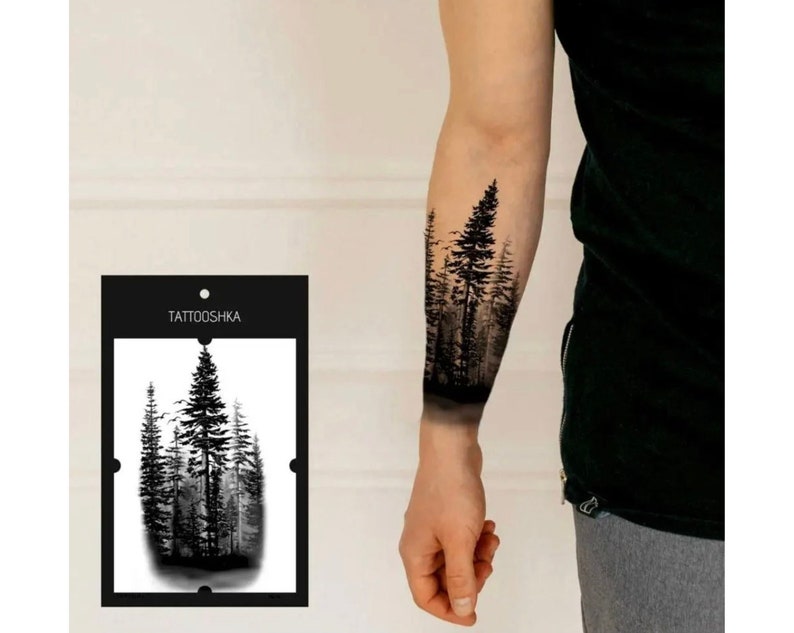 Op de afbeelding: Zwart-wit tijdelijke tattoo met een boslandschap op een arm. Het tattoo-ontwerp toont hoge bomen en een mistige achtergrond. De productverpakking, met het label "TATTOOSHKА", is zichtbaar.