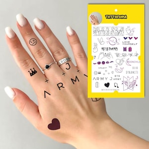 May include: A hand with temporary tattoos of the Korean pop group BTS. The tattoos include the group's name, logos, and song titles, such as "Love Yourself", "Nevermind", "Dynamite", and "Micorcosmos".