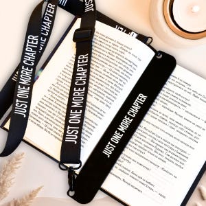 Puede incluir: Juego de cordón y marcapáginas negros con el texto blanco « JUST ONE MORE CHAPTER ». El cordón tiene una hebilla negra ajustable. El marcapáginas está en un libro abierto.