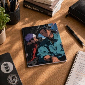 May include: A notebook featuring an anime-style illustration of two characters. One has white hair and sunglasses, the other has black hair and a blue shirt. The notebook is on a wooden surface with other stationery items.