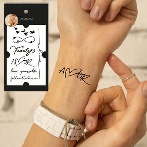 Op de afbeelding: Een tijdelijke tattoo met het woord "AMOR" geschreven in cursief met een hart in plaats van de "O". De tattoo zit op de pols van een persoon.