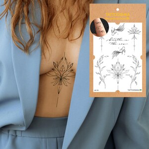 May include: A temporary tattoo sheet with various black line art designs, including floral and botanical elements, and the phrase "breathe in the now." The designs are displayed on a brown backing card. A tattoo is visible on the skin.