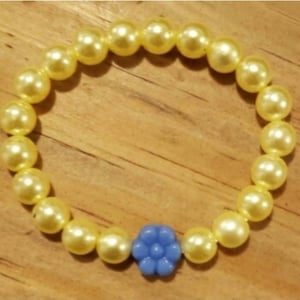 May include: A yellow pearl bracelet with a blue flower charm.