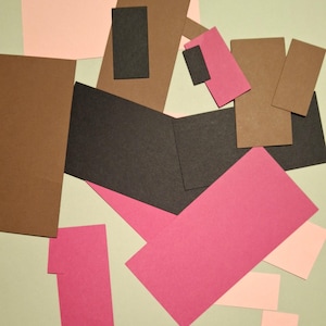 May include: A collection of paper squares in various colors, including pink, brown, and black. The squares are arranged in a random pattern on a light green surface.