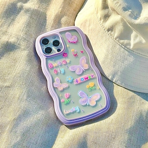 Op de afbeelding: Een transparante telefoonhoes met een paarse rand en een ontwerp van vlinders, bloemen en de tekst "Butter fly at flower" en "lucky".